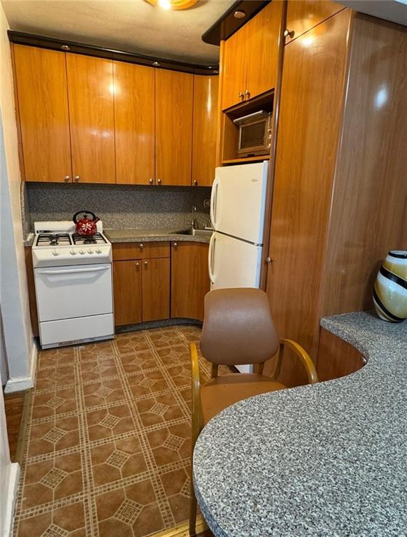 kitchen featuring tasteful backsplash, brown cabinets, white appliances, and a sink