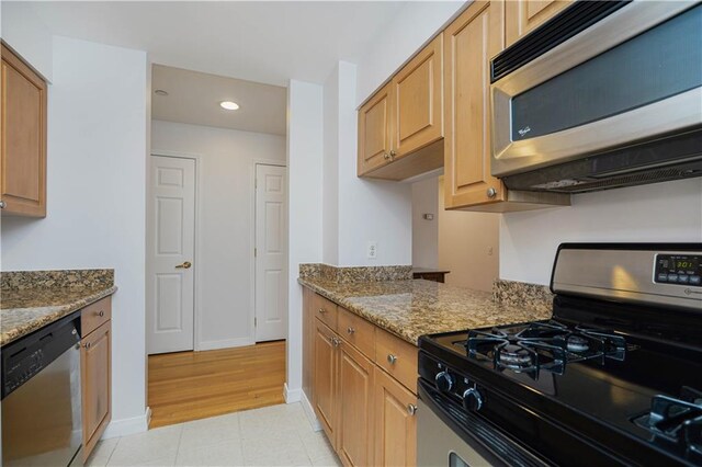 kitchen with stainless steel appliances, light tile patterned floors, and dark stone counters