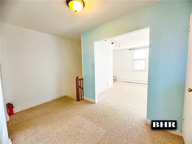 empty room with baseboard heating, carpet, and track lighting