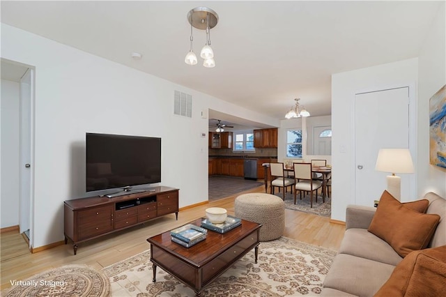 living room with ceiling fan with notable chandelier and light hardwood / wood-style flooring