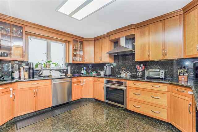 kitchen featuring tasteful backsplash, appliances with stainless steel finishes, wall chimney range hood, and dark stone counters