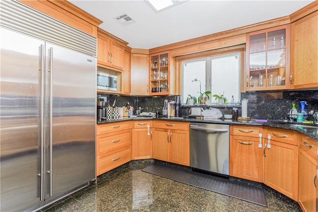 kitchen with dark stone counters, built in appliances, sink, and backsplash