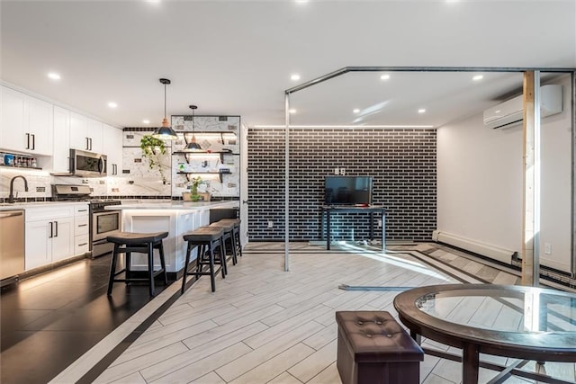 interior space with stainless steel appliances, a kitchen breakfast bar, a wall mounted air conditioner, white cabinets, and decorative light fixtures