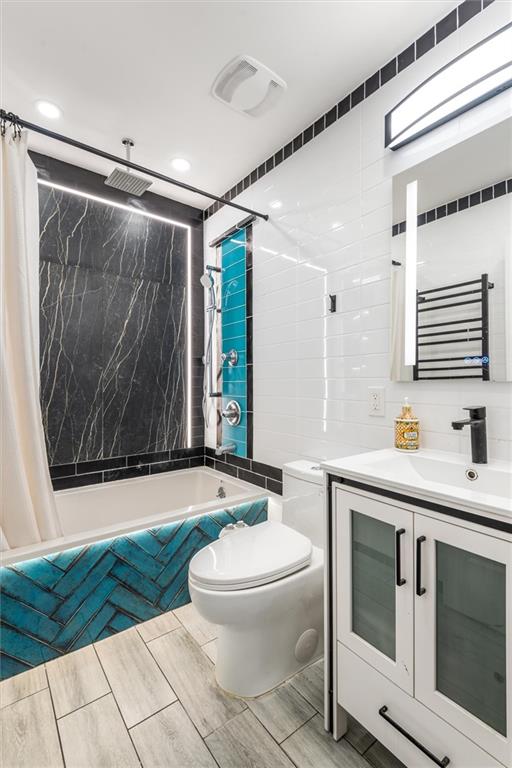 full bathroom featuring radiator heating unit, tile walls, vanity, toilet, and shower / bath combo