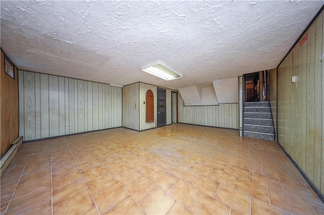 basement featuring wooden walls, light tile patterned floors, and a textured ceiling