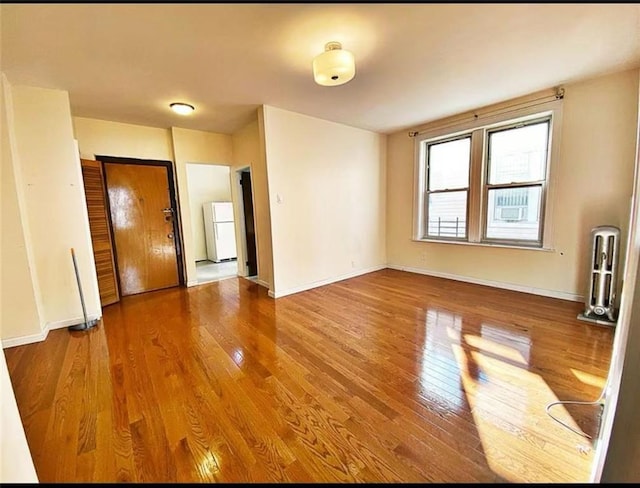 unfurnished room with radiator, baseboards, and wood-type flooring