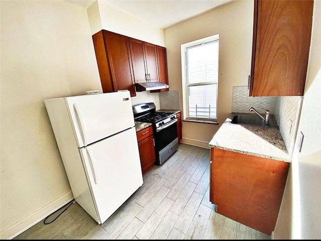 kitchen with under cabinet range hood, a sink, tasteful backsplash, freestanding refrigerator, and gas stove