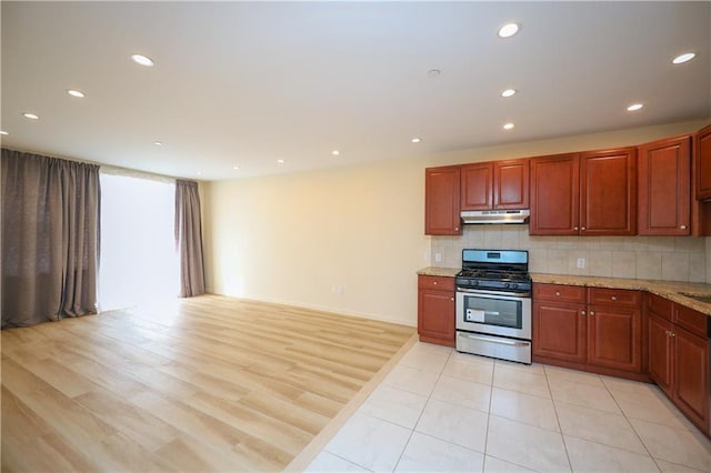 kitchen with stainless steel gas stove, light stone counters, light wood-type flooring, and tasteful backsplash