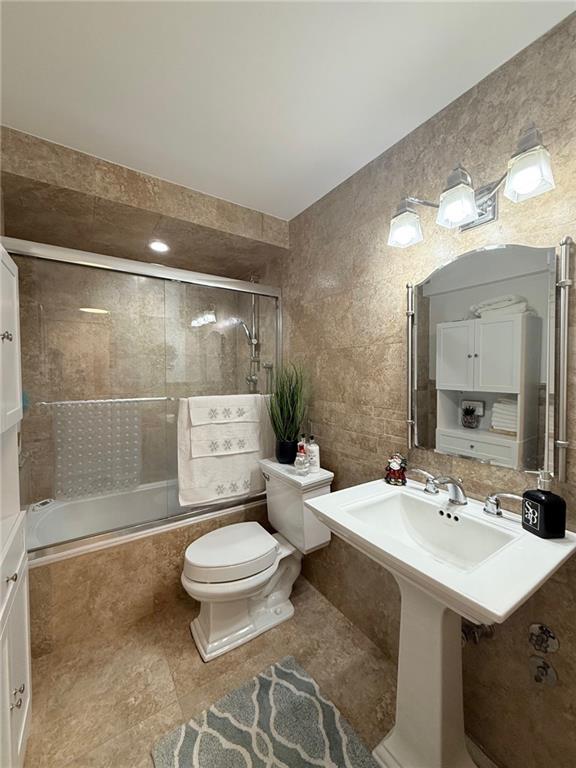 bathroom with toilet, shower / bath combination with glass door, and tile walls