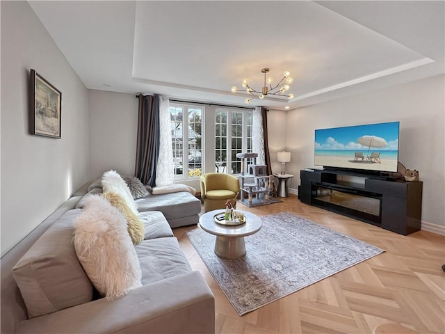 living room with baseboards, a glass covered fireplace, a raised ceiling, and a notable chandelier