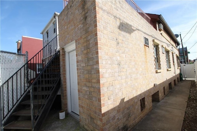 view of property exterior with stairs, fence, and brick siding