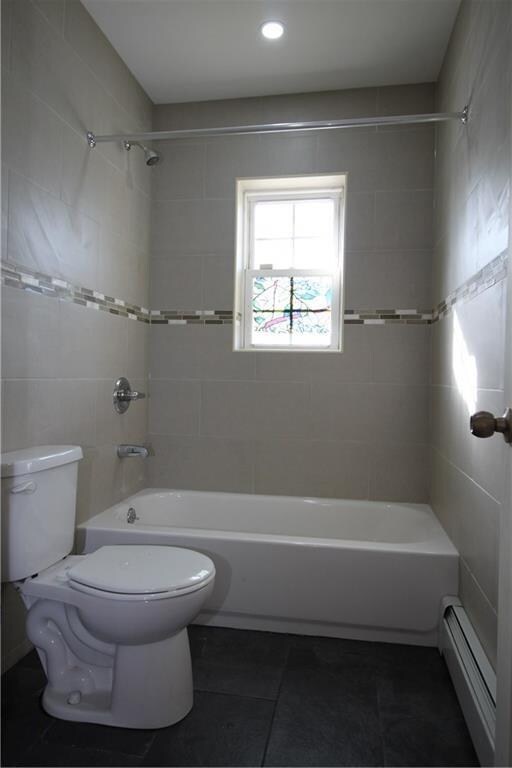 bathroom with tiled shower / bath combo, a baseboard radiator, tile patterned floors, and toilet