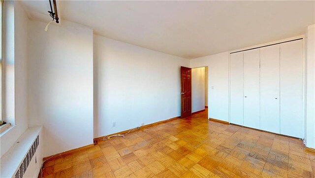 unfurnished bedroom featuring radiator, a closet, rail lighting, and light parquet floors