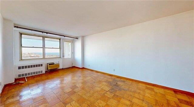 spare room featuring a wall mounted air conditioner, radiator heating unit, and light parquet floors