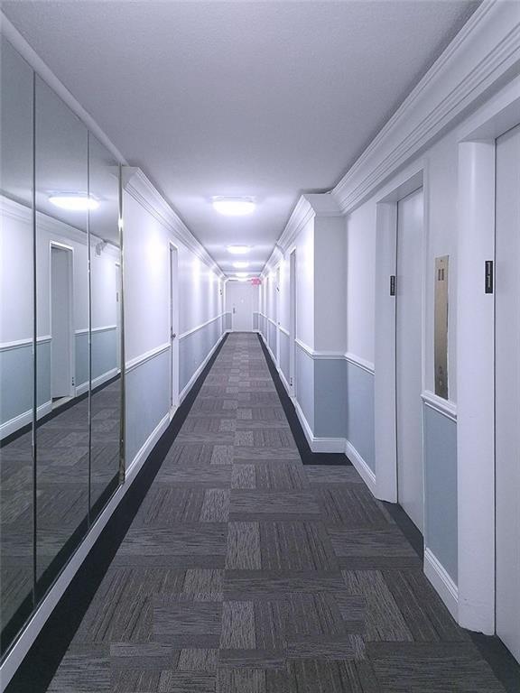 hallway with crown molding and dark carpet