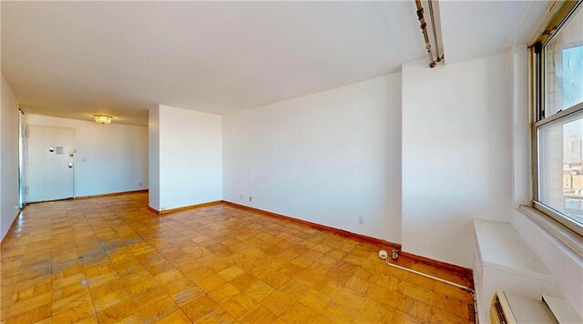 unfurnished room featuring light parquet flooring, a baseboard heating unit, and track lighting