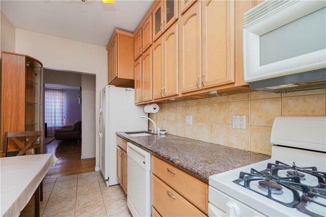 kitchen with tasteful backsplash, sink, dark stone counters, light tile patterned floors, and white appliances