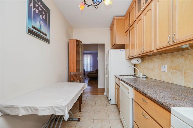 kitchen with light tile patterned floors, sink, dishwasher, dark stone countertops, and light brown cabinets