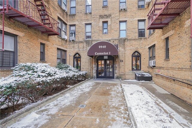 snow covered property entrance featuring french doors and cooling unit