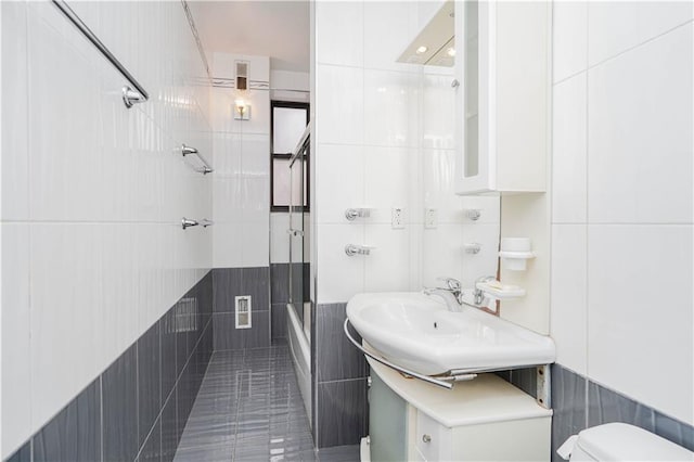 full bathroom with tile walls, sink, bath / shower combo with glass door, and tile patterned floors