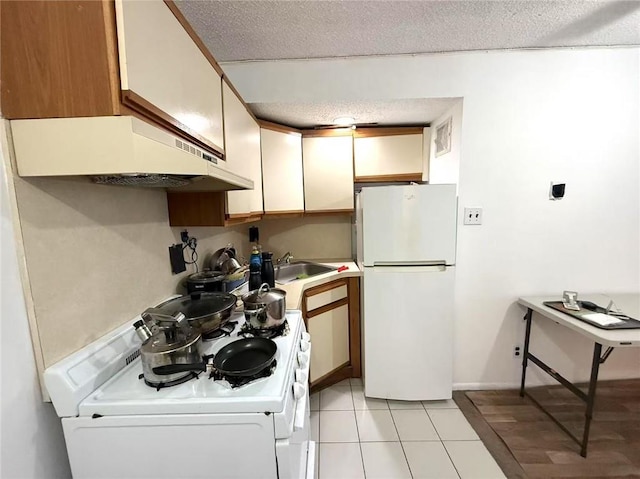 kitchen with sink, white appliances, white cabinets, a textured ceiling, and light tile patterned flooring