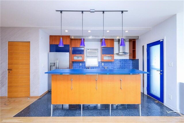 kitchen with wall chimney range hood, decorative light fixtures, a center island, and stainless steel counters