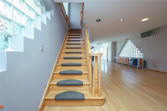 staircase featuring an AC wall unit, a healthy amount of sunlight, and hardwood / wood-style floors