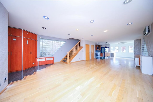 unfurnished living room featuring a wall mounted air conditioner and light hardwood / wood-style flooring