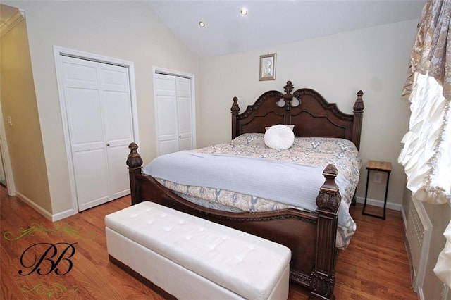 bedroom with wood finished floors, vaulted ceiling, baseboards, and two closets