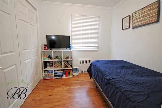 bedroom with wood finished floors, radiator heating unit, a closet, and crown molding