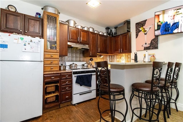 kitchen with backsplash, a kitchen bar, kitchen peninsula, dark wood-type flooring, and white appliances