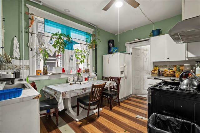 kitchen with ventilation hood, white cabinetry, black range with gas stovetop, hardwood / wood-style flooring, and white refrigerator with ice dispenser