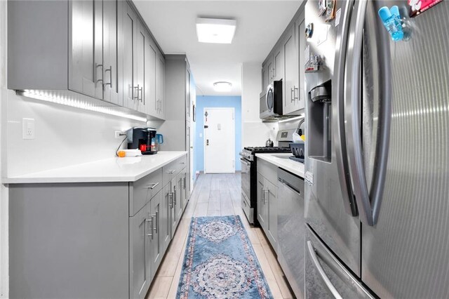 kitchen with appliances with stainless steel finishes, gray cabinetry, and light hardwood / wood-style flooring