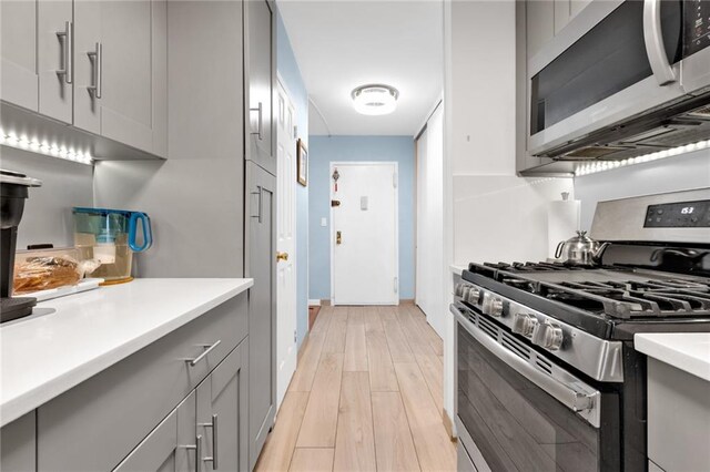 kitchen with appliances with stainless steel finishes, gray cabinetry, and light wood-type flooring