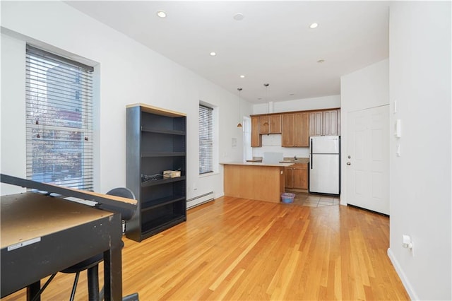 kitchen with refrigerator, decorative light fixtures, a baseboard radiator, kitchen peninsula, and light wood-type flooring