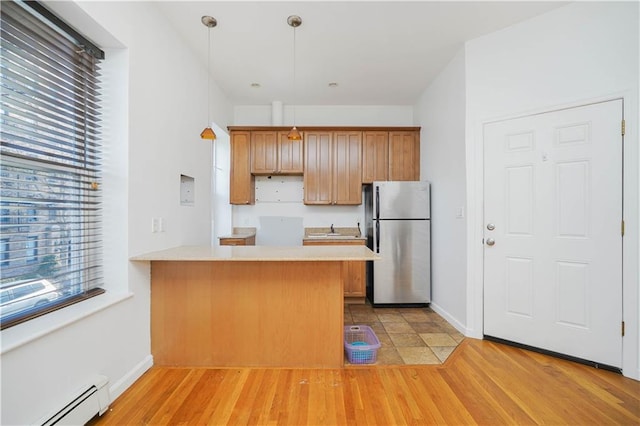 kitchen with hanging light fixtures, light hardwood / wood-style flooring, stainless steel refrigerator, a baseboard radiator, and kitchen peninsula