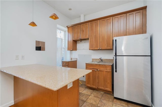 kitchen with sink, light stone counters, stainless steel fridge, kitchen peninsula, and pendant lighting