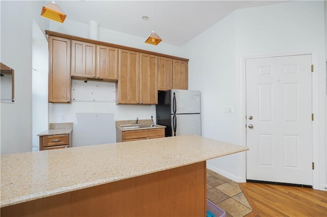 kitchen featuring light stone countertops, fridge, sink, and light hardwood / wood-style floors