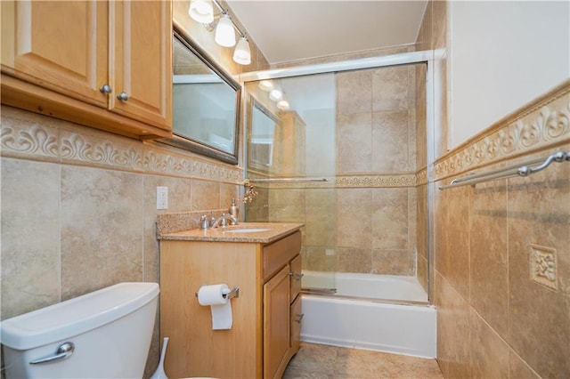 full bathroom featuring toilet, vanity, bath / shower combo with glass door, and tile walls