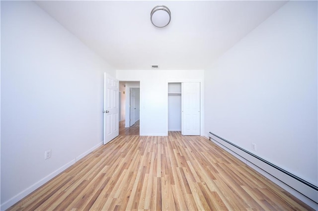 unfurnished bedroom featuring a baseboard heating unit, light hardwood / wood-style flooring, and a closet