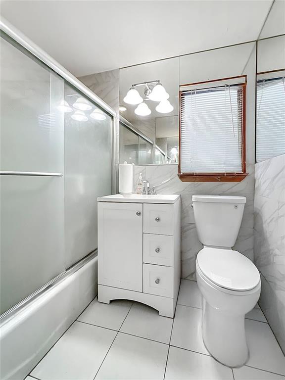 full bathroom with enclosed tub / shower combo, tile patterned flooring, tile walls, vanity, and toilet