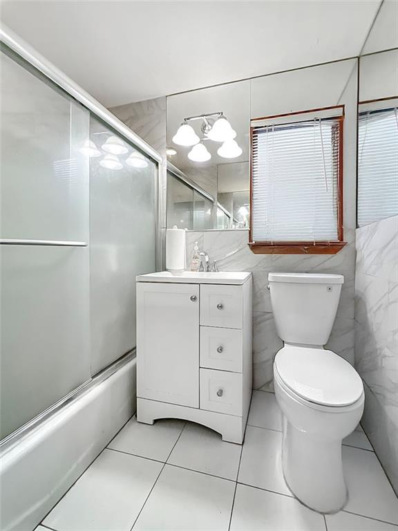 bathroom with vanity, shower / bath combination with glass door, toilet, tile walls, and tile patterned floors