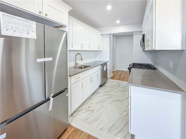 kitchen with stainless steel appliances, white cabinetry, sink, and dark stone counters