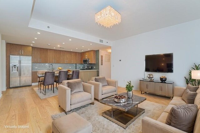 living room featuring an inviting chandelier, sink, and light wood-type flooring