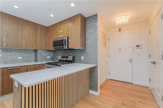 kitchen featuring appliances with stainless steel finishes, kitchen peninsula, light hardwood / wood-style floors, and decorative backsplash