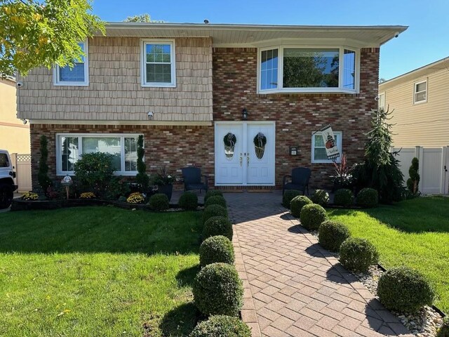 view of front of property with brick siding, a front lawn, and fence