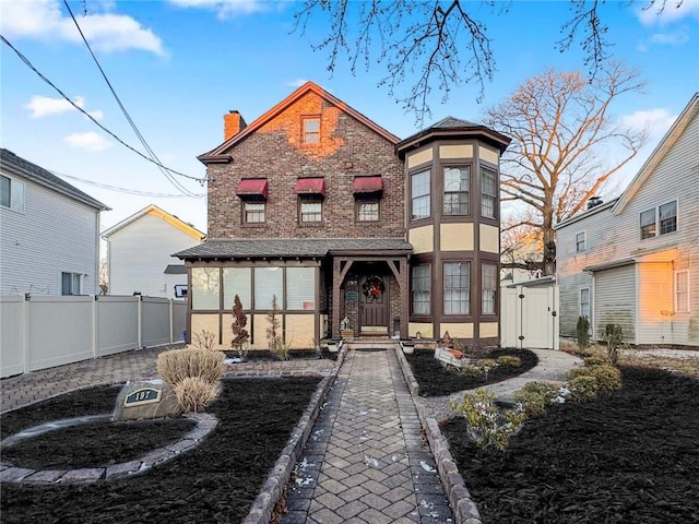 view of front of property with brick siding, a chimney, and fence