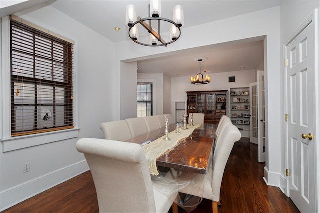 dining space featuring dark wood-style floors, a notable chandelier, and baseboards