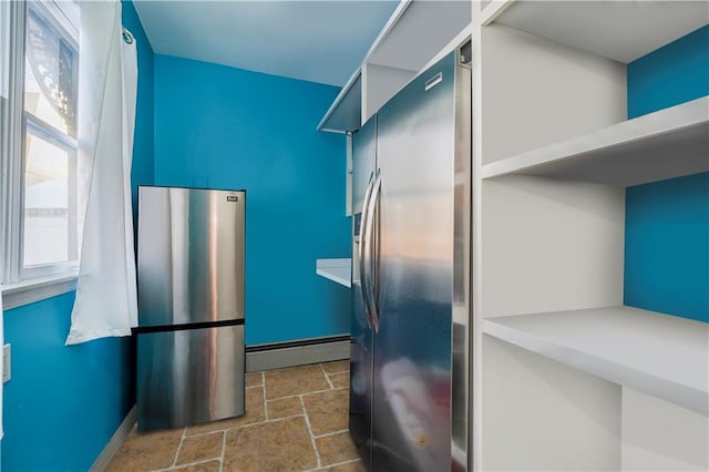 kitchen featuring a baseboard heating unit, baseboards, stone tile floors, freestanding refrigerator, and stainless steel fridge