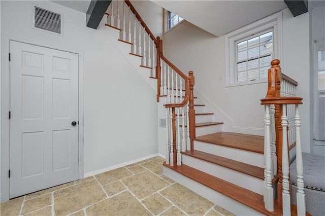 stairs with a wealth of natural light, visible vents, baseboards, and stone tile flooring